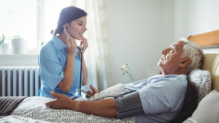 female nurse taking the blood pressure and heartbeat of an elderly man laying down in bed