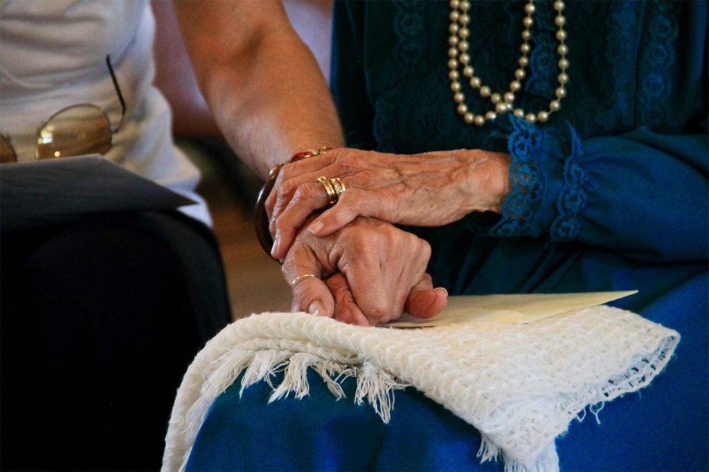 carer holding hands with an elderly lady in support