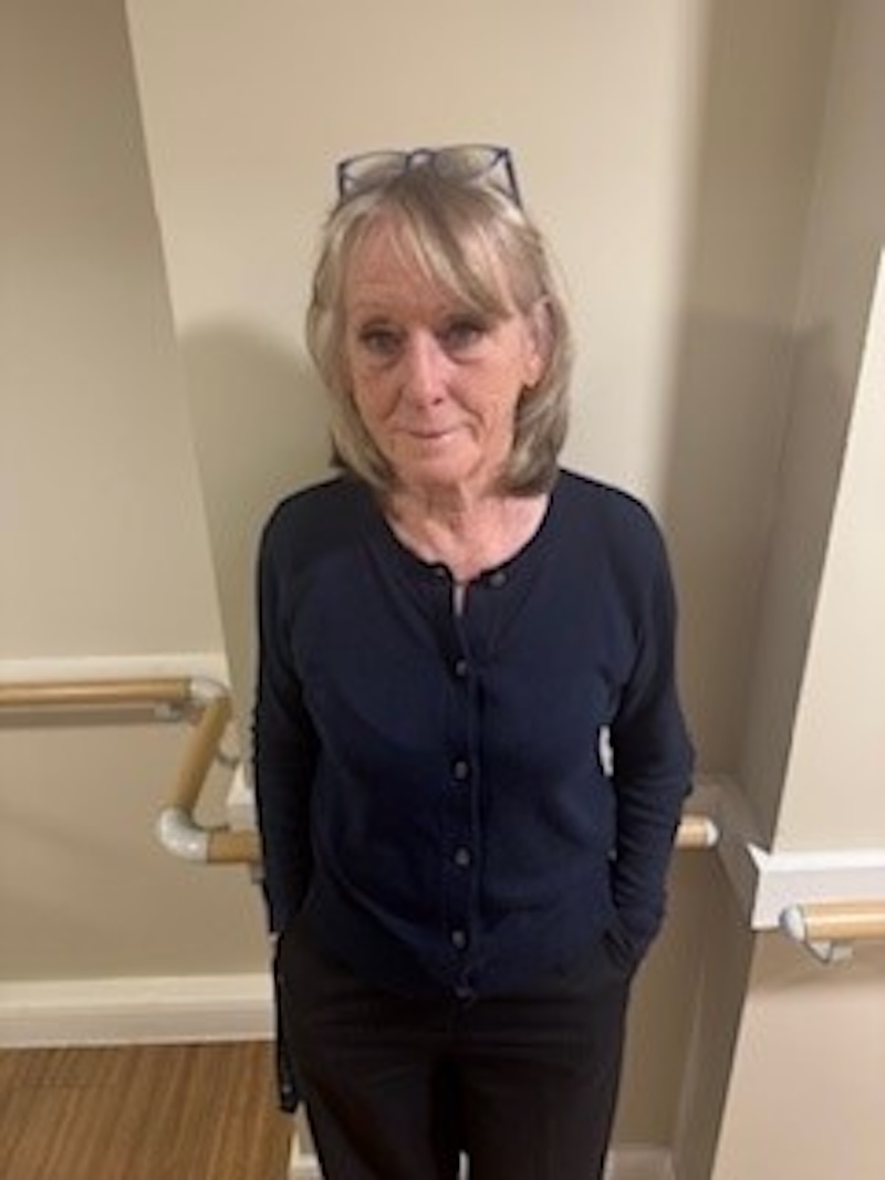 woman with blonde hair wearing a dark blue cardigan stood in front of plain wall having her photo taken for the team page