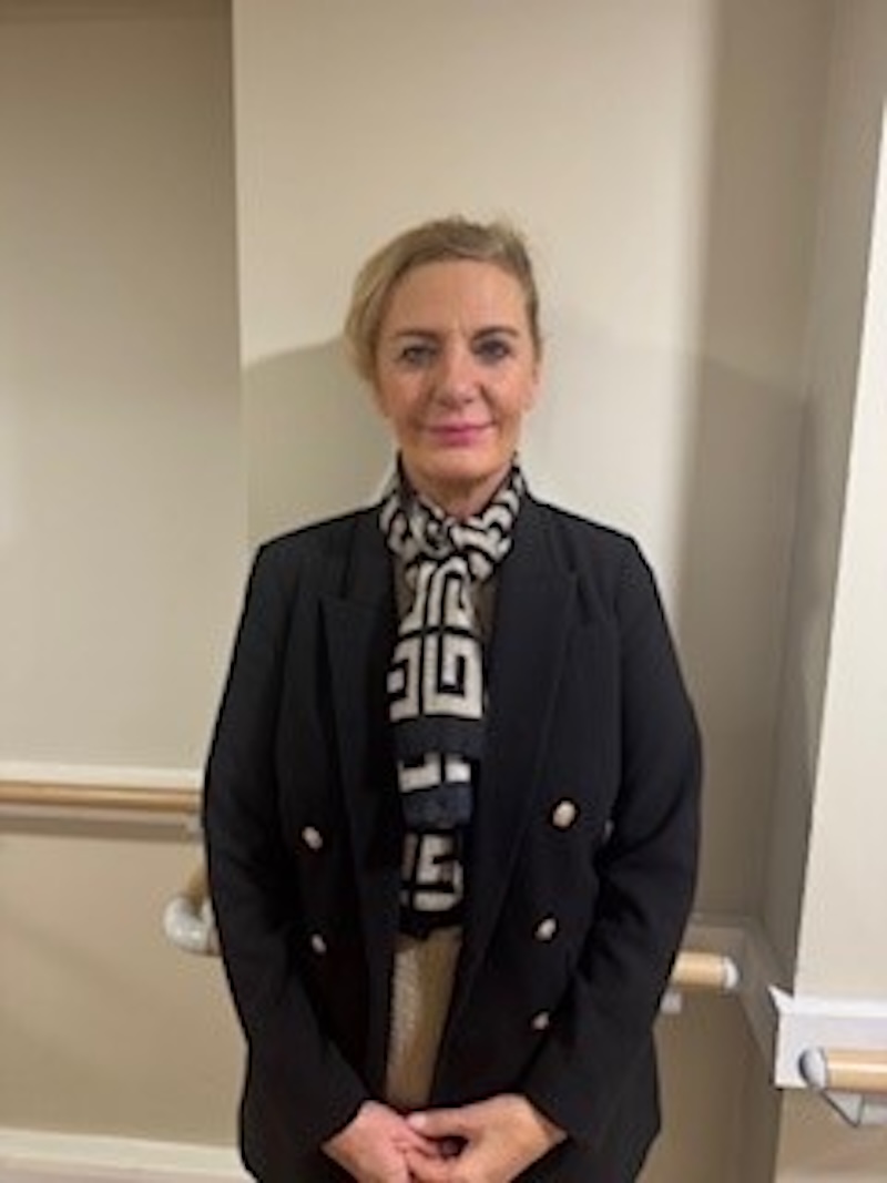 woman with blonde hair wearing a black blazer stood in front of plain wall having her photo taken for the team page