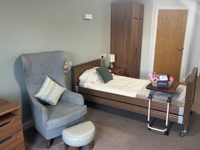 A bedroom with a profiling bed and an armchair and foot stall next to it