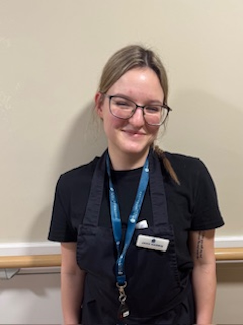 woman with blonde hair wearing a dark blue uniform stood in front of plain wall having her photo taken for the team page