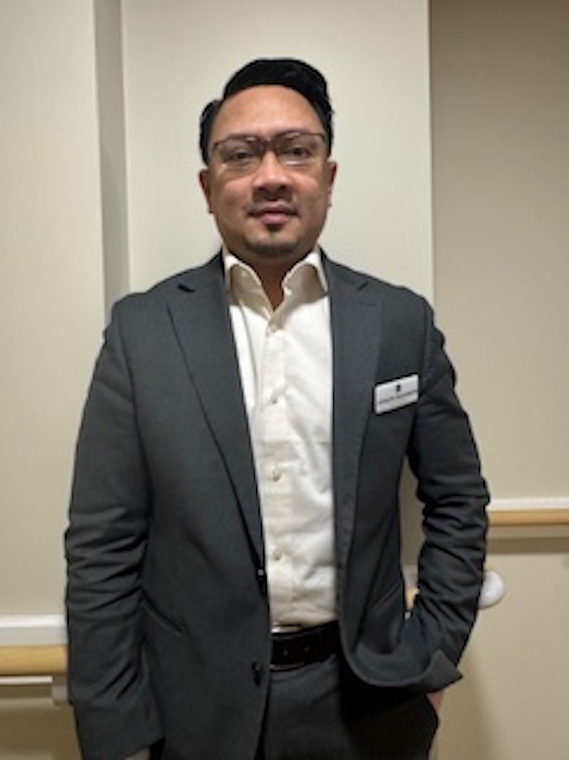 man with brown hair wearing a suit stood in front of a plain wall having his photo taken for the team page