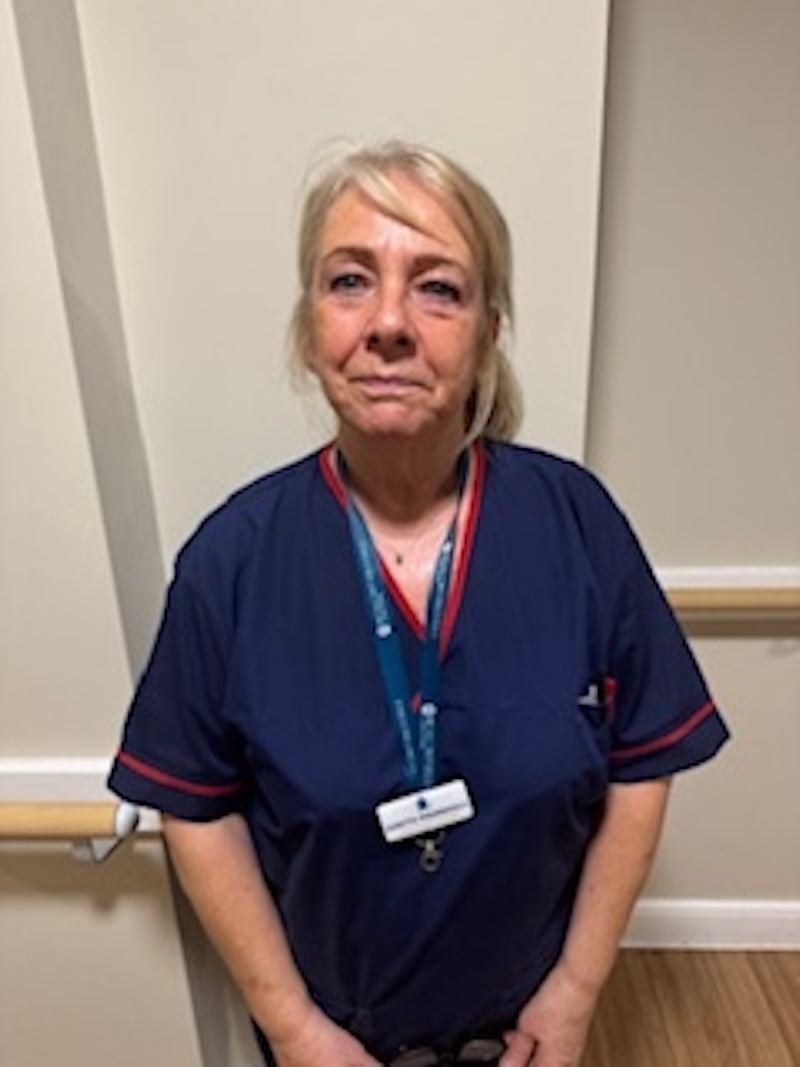 woman with blonde hair wearing a dark blue uniform stood in front of plain wall having her photo taken for the team page