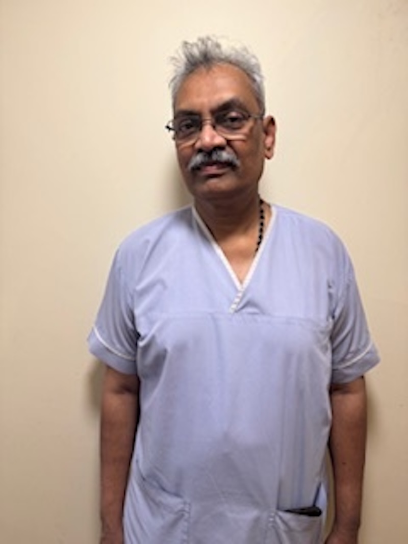 man wearing a lilac uniform stood in front of plain wall having his photo taken for the team page