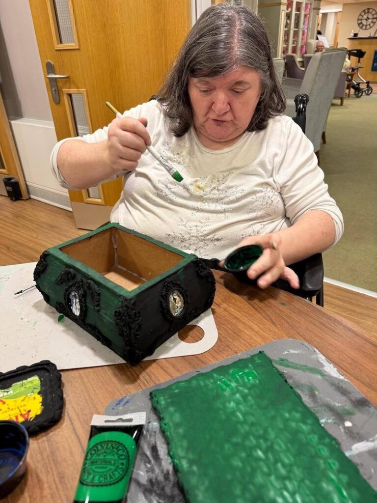 female care home resident with a white top on painting a green and black box
