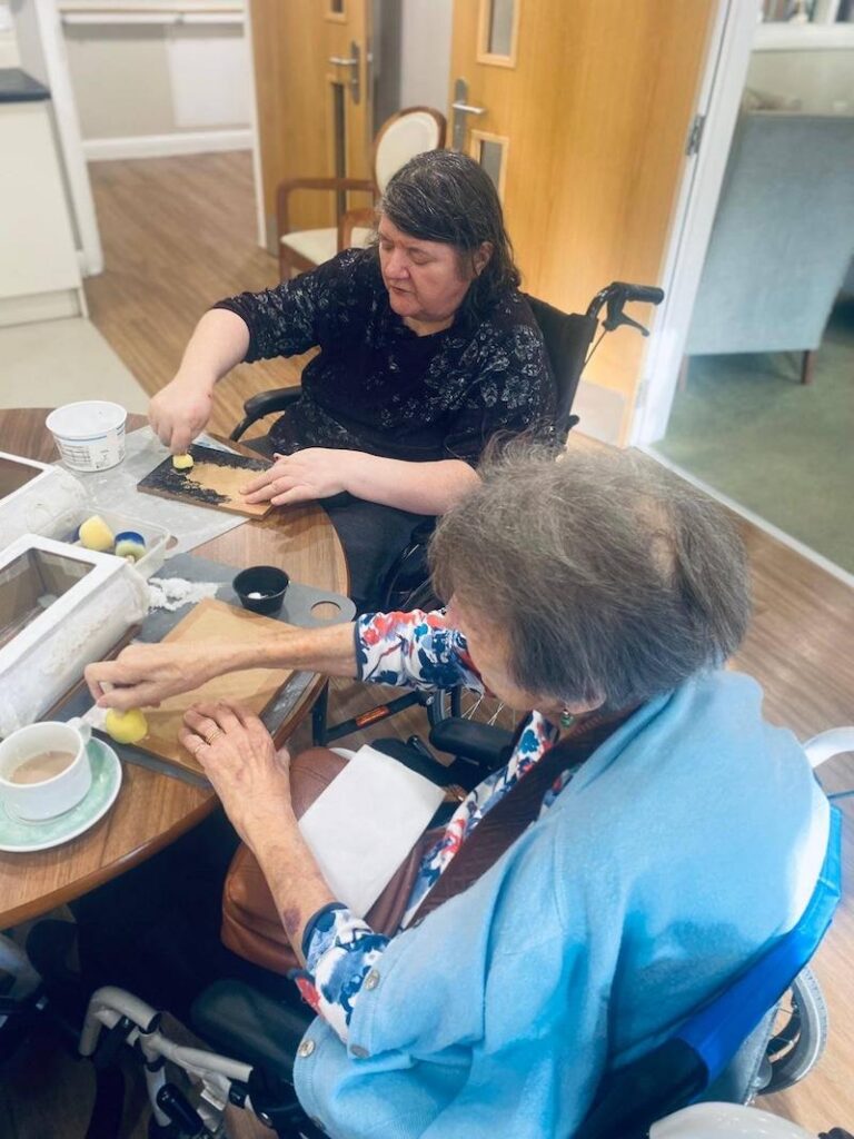 two elderly women sat at a table doing arts and crafts together