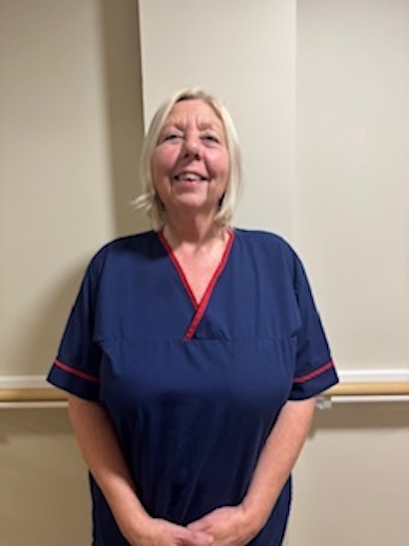 woman with blonde hair wearing a dark blue uniform stood in front of plain wall having her photo taken for the team page