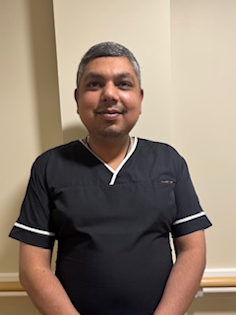 man wearing a black housekeeping uniform stood in front of a plain wall having his photo taken for the team page