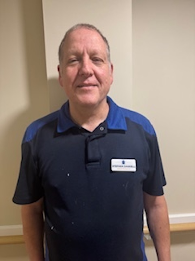 man wearing a navy top stood in front of a plain wall having his photo taken for the team page