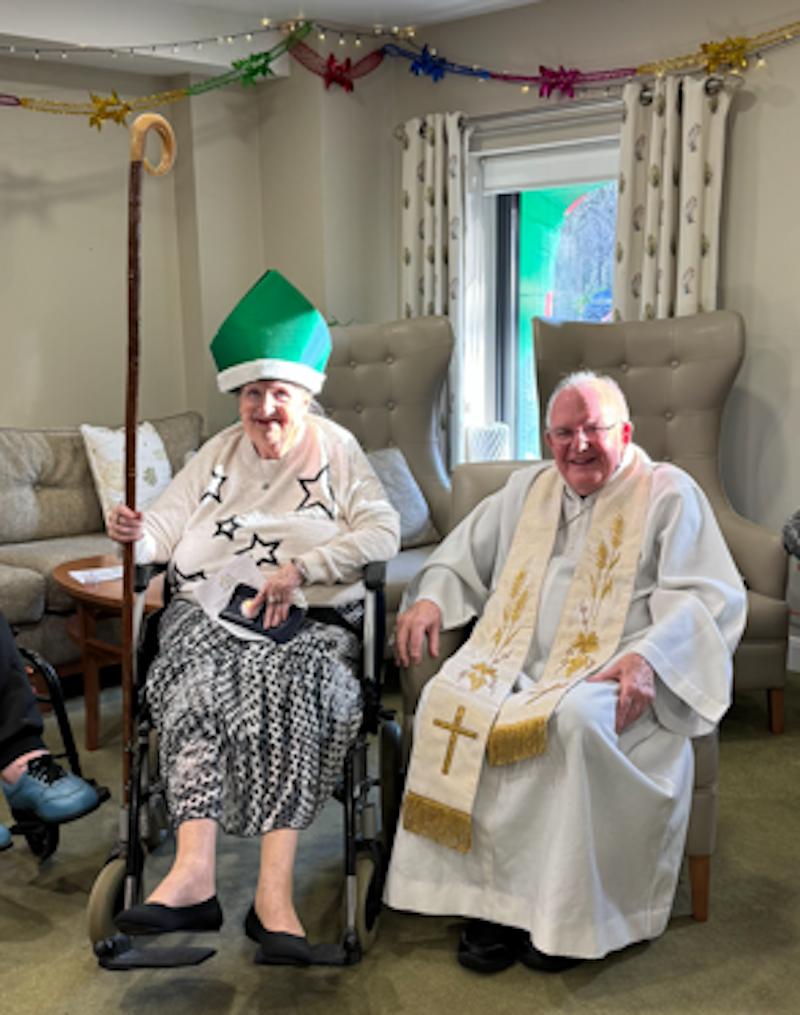 female resident sat in a wheelchair next to father patrick in the lounge