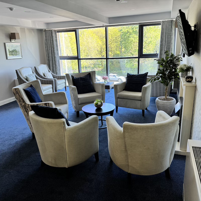 armchairs set in a circle with sofas behind next to the bright windows showing woodland outside on the residential floor