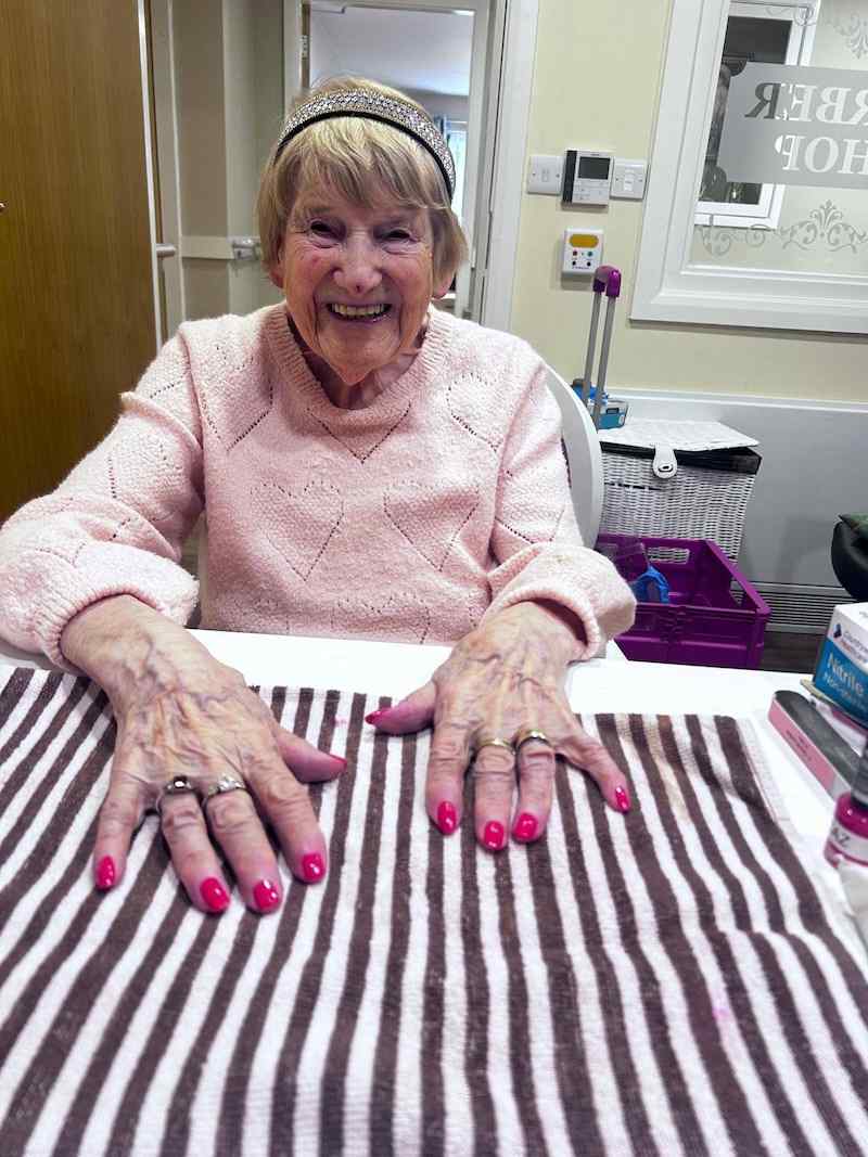 elderly woman sat down smiling showing off her painted nails